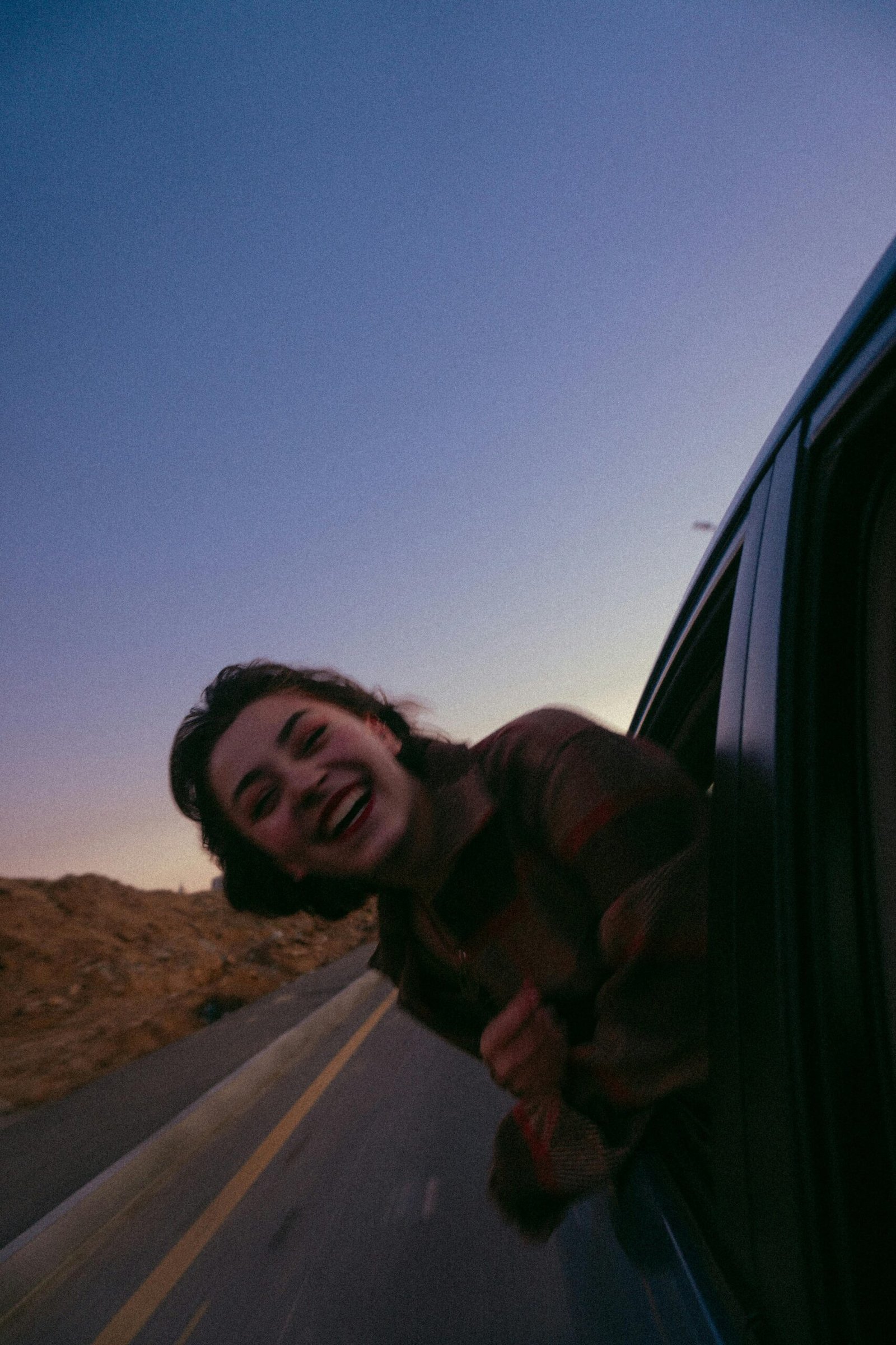 A girl leans out of a car window smiling during a sunset road trip in Baku, capturing a moment of joy and freedom.